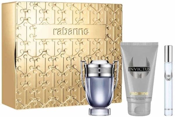Rabanne Invictus gift set displayed in front of a gold embossed box. The set includes the Invictus trophy-shaped eau de toilette bottle, a grey Invictus body lotion, and a small travel spray.